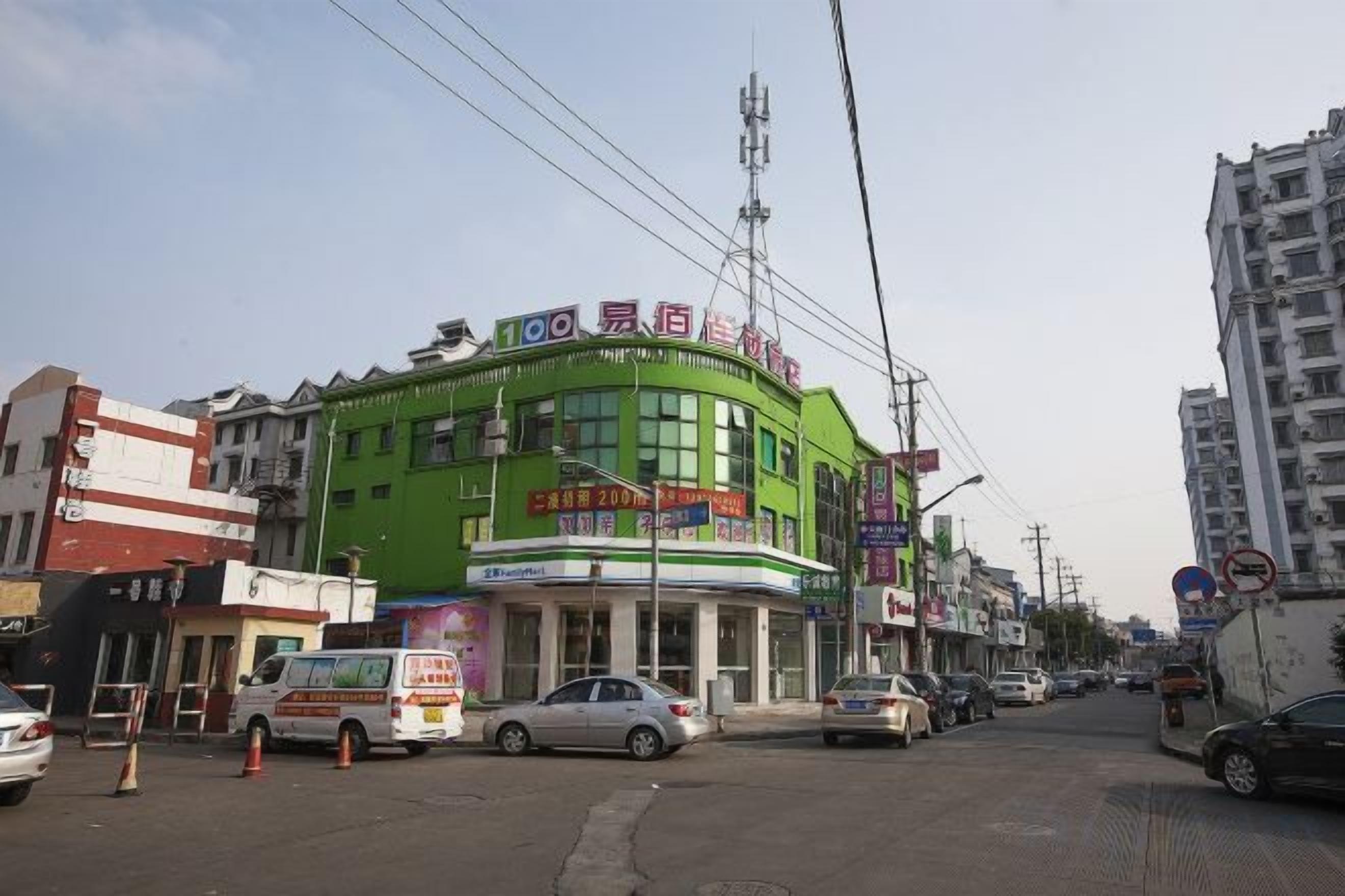 A multi-story building with a green facade, multiple commercial units on the ground floor, and a clear sky.