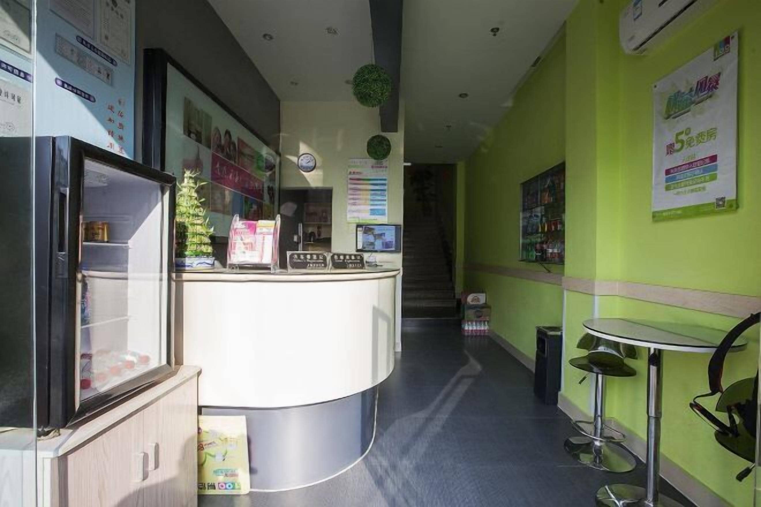 Uma área de recepção com balcão, geladeira, uma pequena planta e um cartaz na parede.