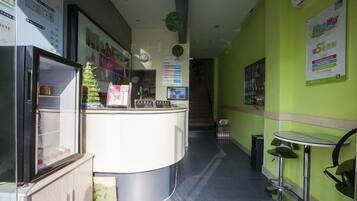 Uma área de recepção com balcão, geladeira, uma pequena planta e um cartaz na parede.