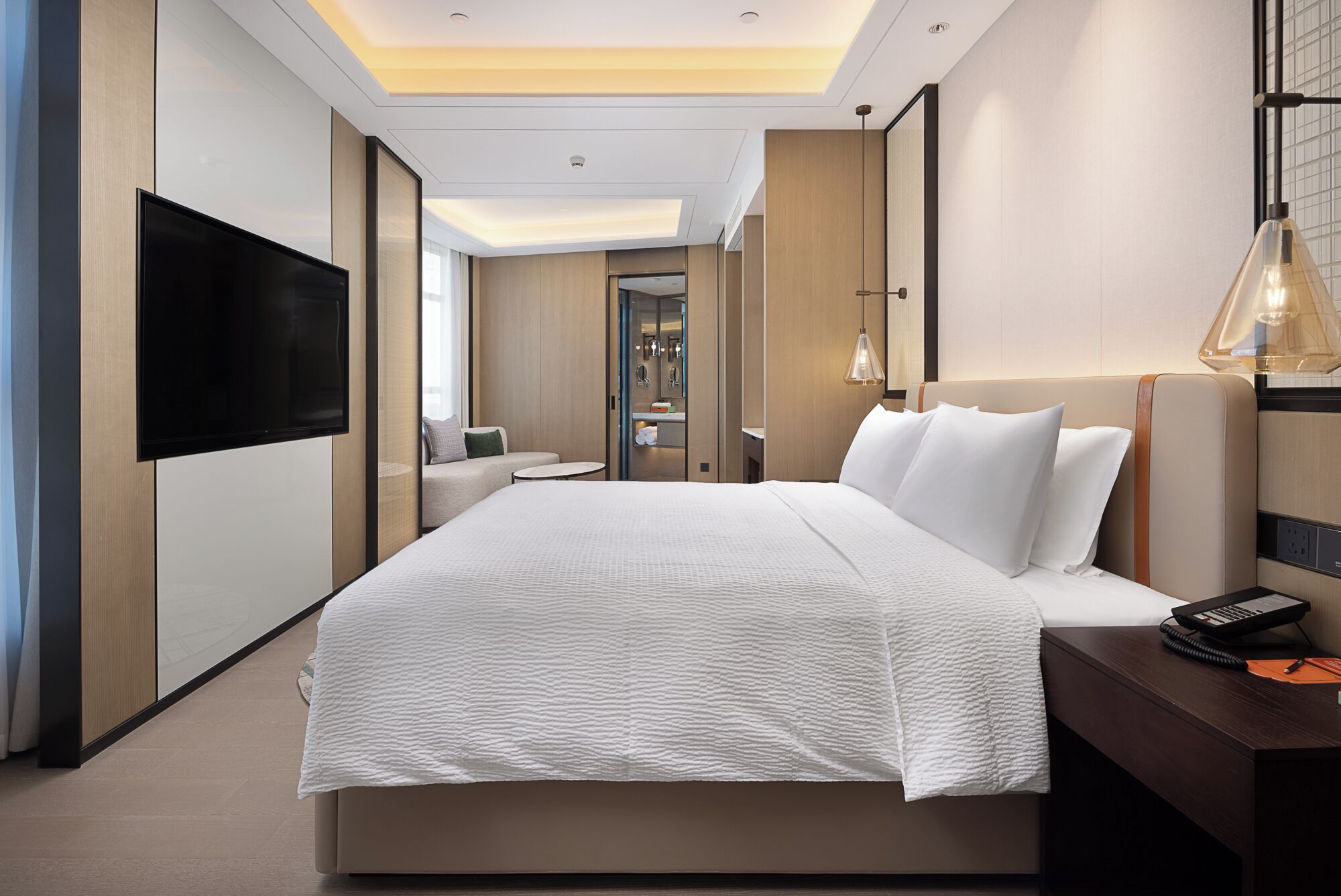 A modern hotel room with a large bed, a flat-screen TV, a bedside table with a lamp, and a view of the bathroom.