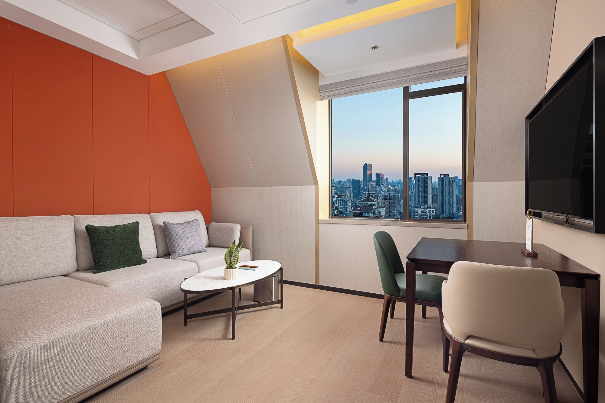 Un salon moderne avec un canapé, une table basse et un coin repas avec des chaises. Une grande fenêtre offre une vue sur la ville.