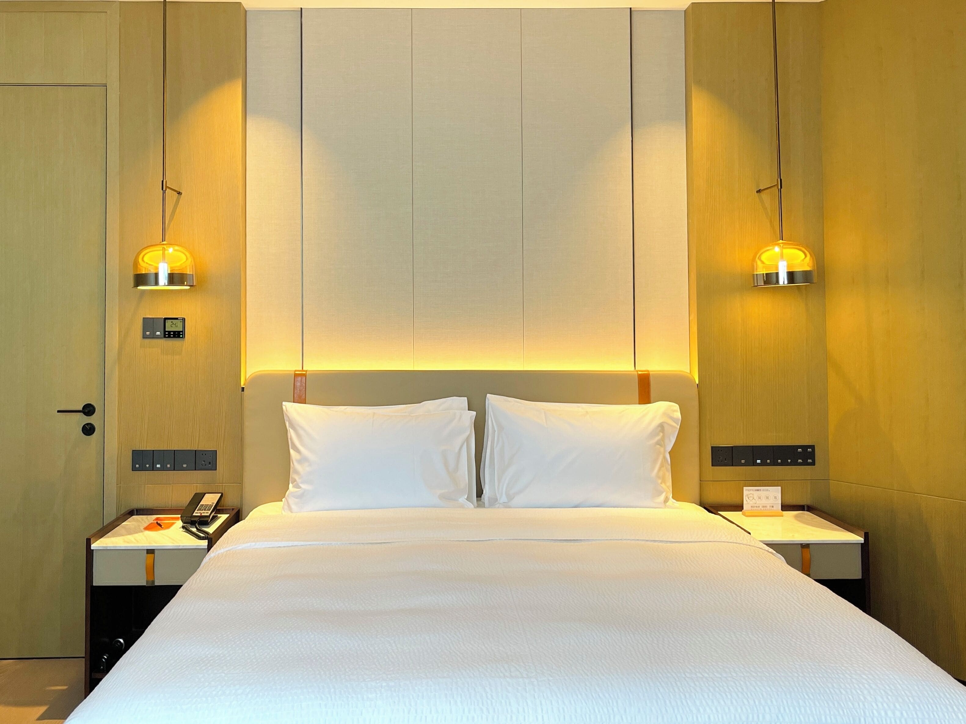 Une chambre d’hôtel avec un grand lit, deux tables de chevet, une commode, un téléphone et des lampes fixées au mur.