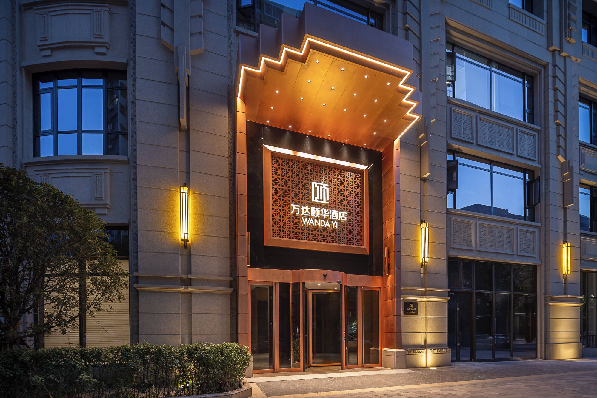 A hotel entrance with a modern design, featuring a prominent illuminated sign and a revolving door.
