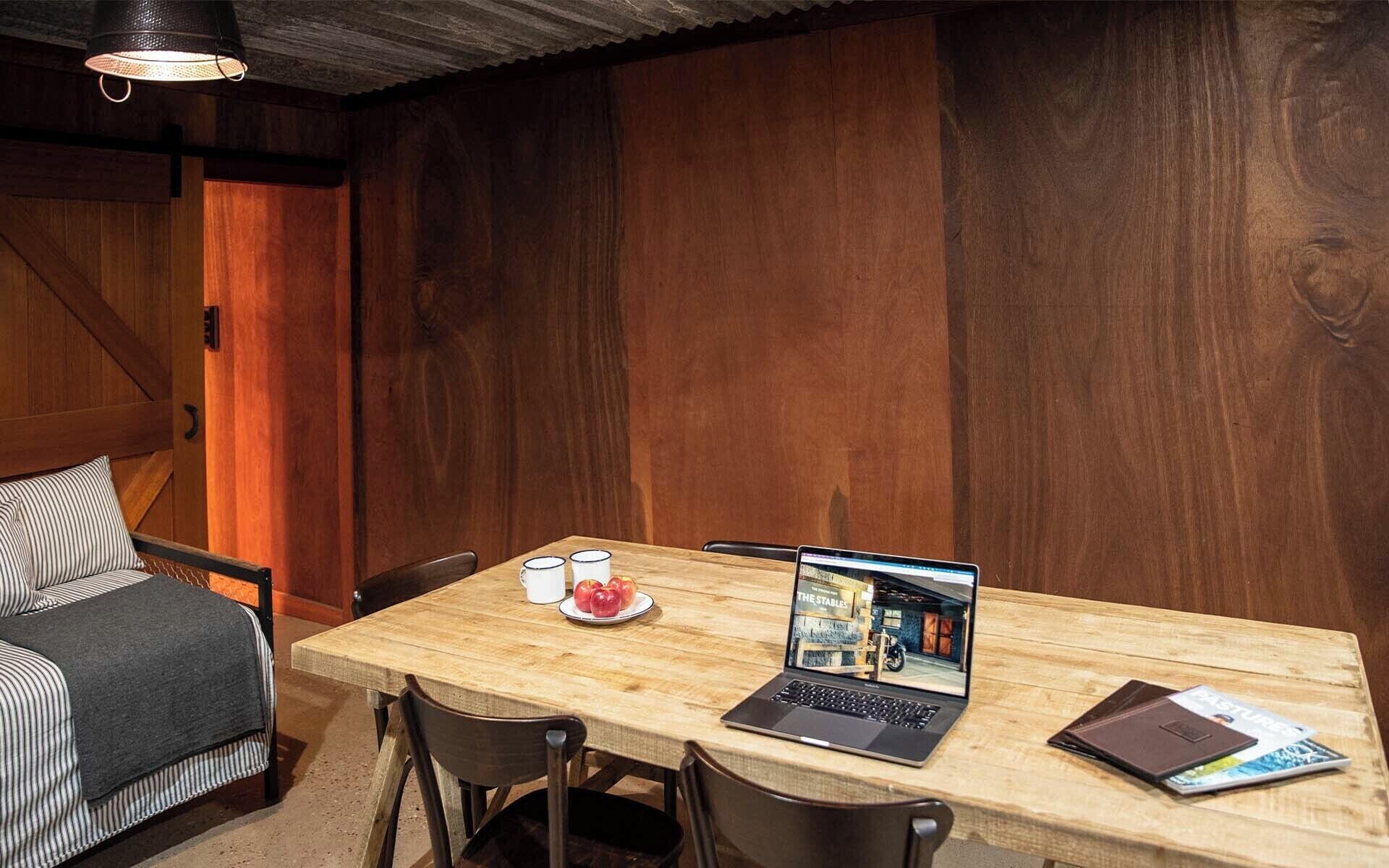A wooden dining table with a laptop, a magazine, and a plate with apples.