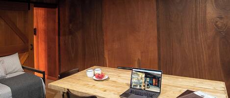 A wooden dining table with a laptop, a magazine, and a plate with apples.