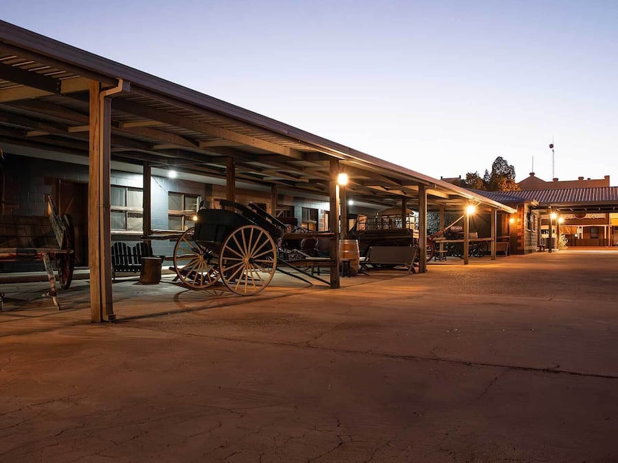 An outdoor historical site with a covered area, a vintage carriage, and a building with a traditional facade.