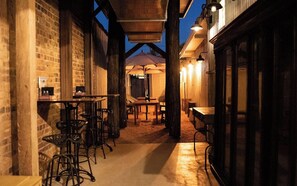 An outdoor corridor with tables and chairs, a brick wall, and a building in the background. - The Staging Post (Longreach)