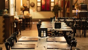 A restaurant with wooden tables and chairs, a vintage espresso machine, and a red window in the background. - The Staging Post (Longreach)