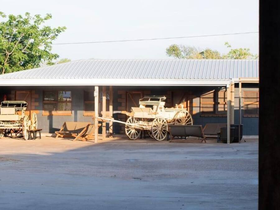 Una construcción rústica con techo de lámina corrugada, vigas de madera y un espacio cubierto con un banco de madera y un carrito.