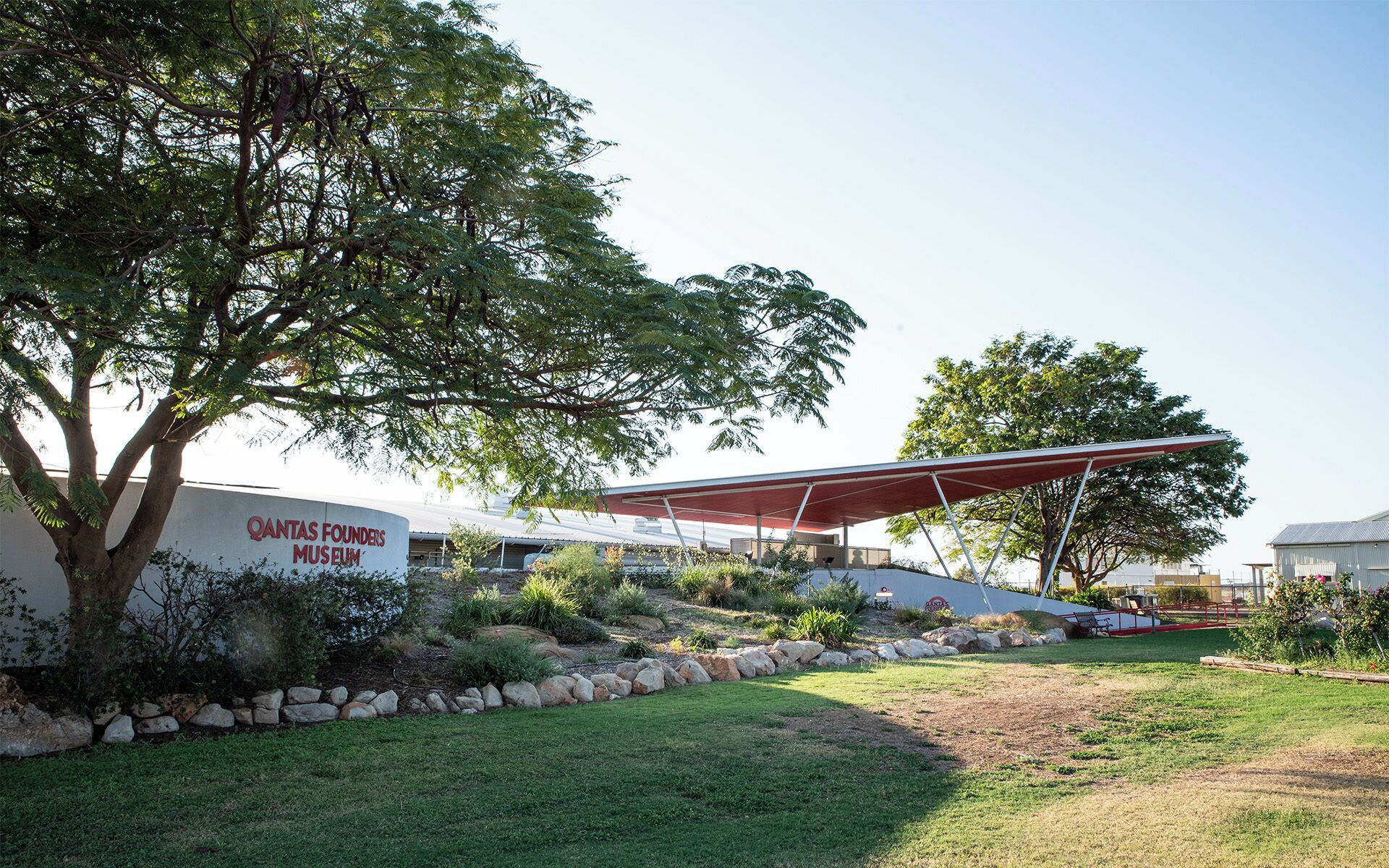 A Qantas Founders Museum with a modern architectural design, featuring a large tree and a covered outdoor area.
