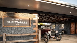 A vintage car parked in front of a building with a sign reading "The Stables." - The Staging Post (Longreach)