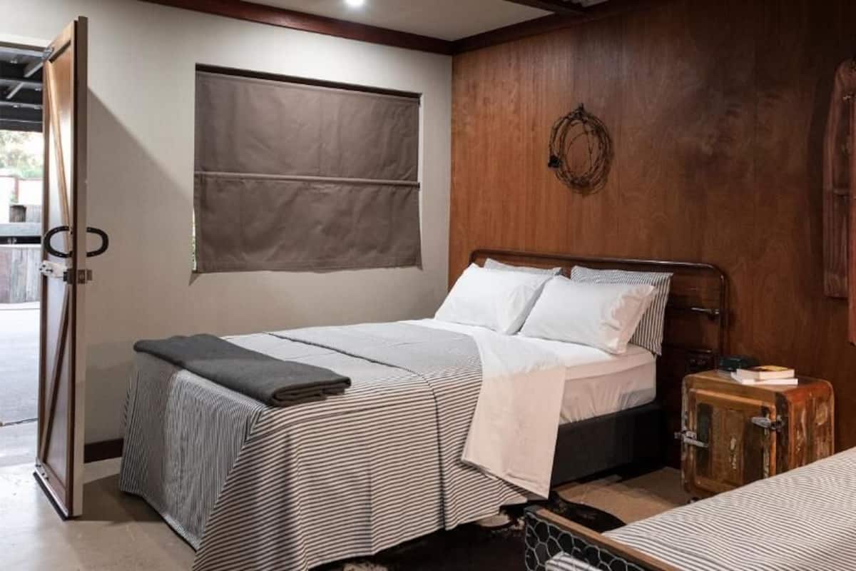 Un dormitorio con cama, una mesita, una maleta y una ventana.