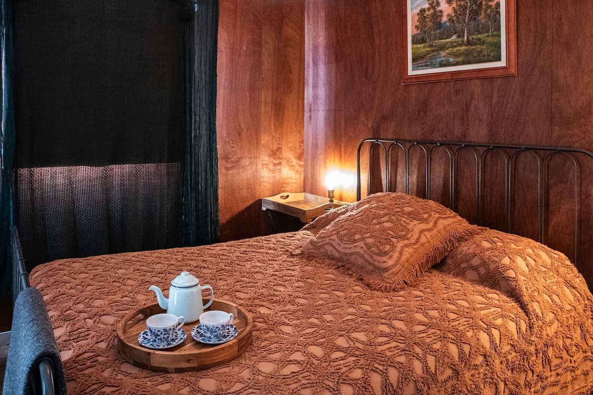 Un dormitorio acogedor con cama, una mesita de noche con lámpara, un cuadro en la pared y una bandeja con tetera y tazas.