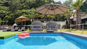 Ein Schwimmbecken mit Liegestühlen und Sonnenschirmen, umgeben von viel Grün.