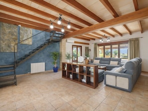 A spacious living room with a staircase, wooden beams, a sofa, a coffee table, and a potted plant. - Son Bosc by Interhome (Inca)
