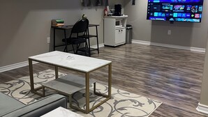 A modern living room with a flat-screen TV mounted on the wall, a coffee machine, and a small table with chairs.