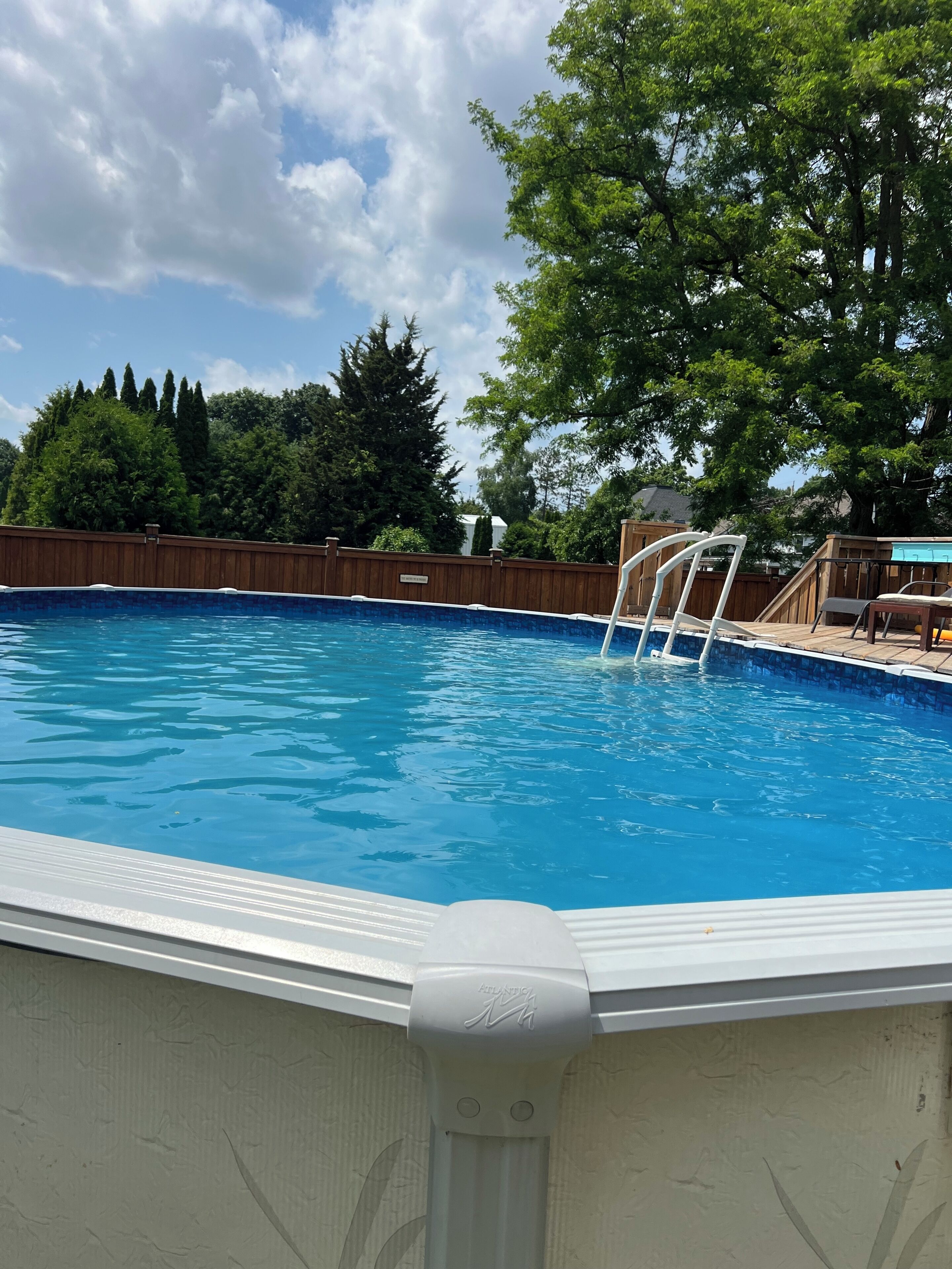 A rectangular swimming pool with a wooden deck and a white ladder.
