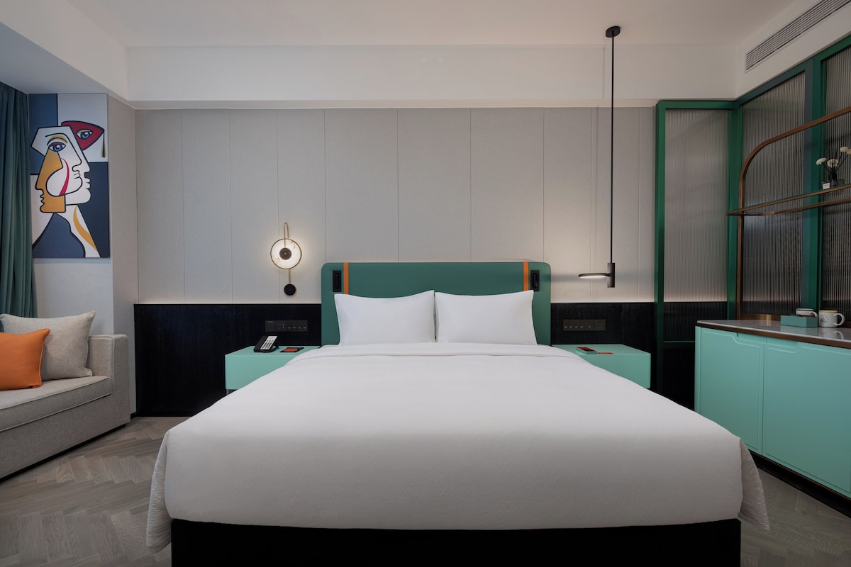 A modern hotel room with a large bed, a desk, and a seating area.