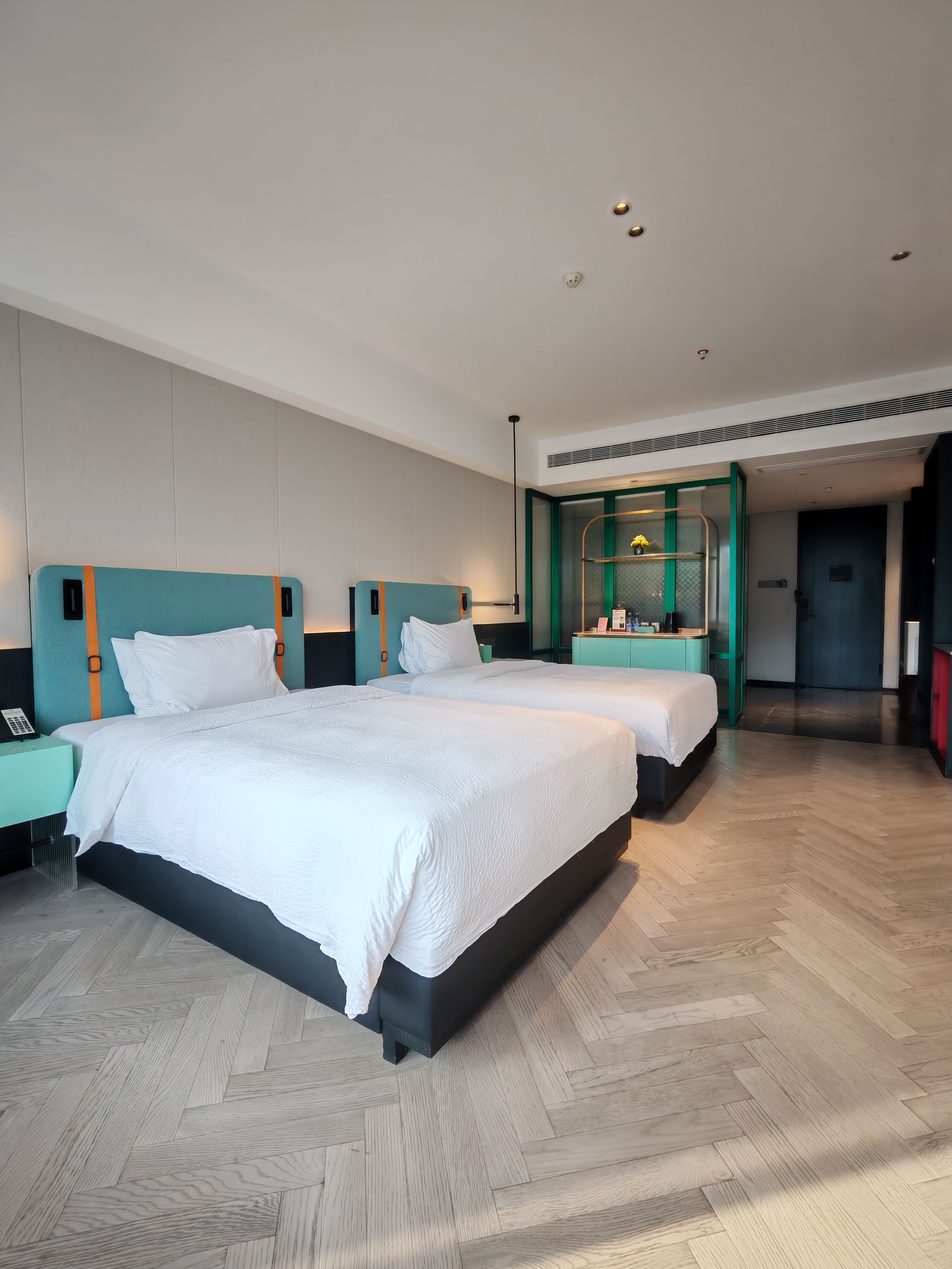 Habitación de hotel con dos camas, una mesita de noche, un escritorio y un baño visible a través de una puerta abierta.