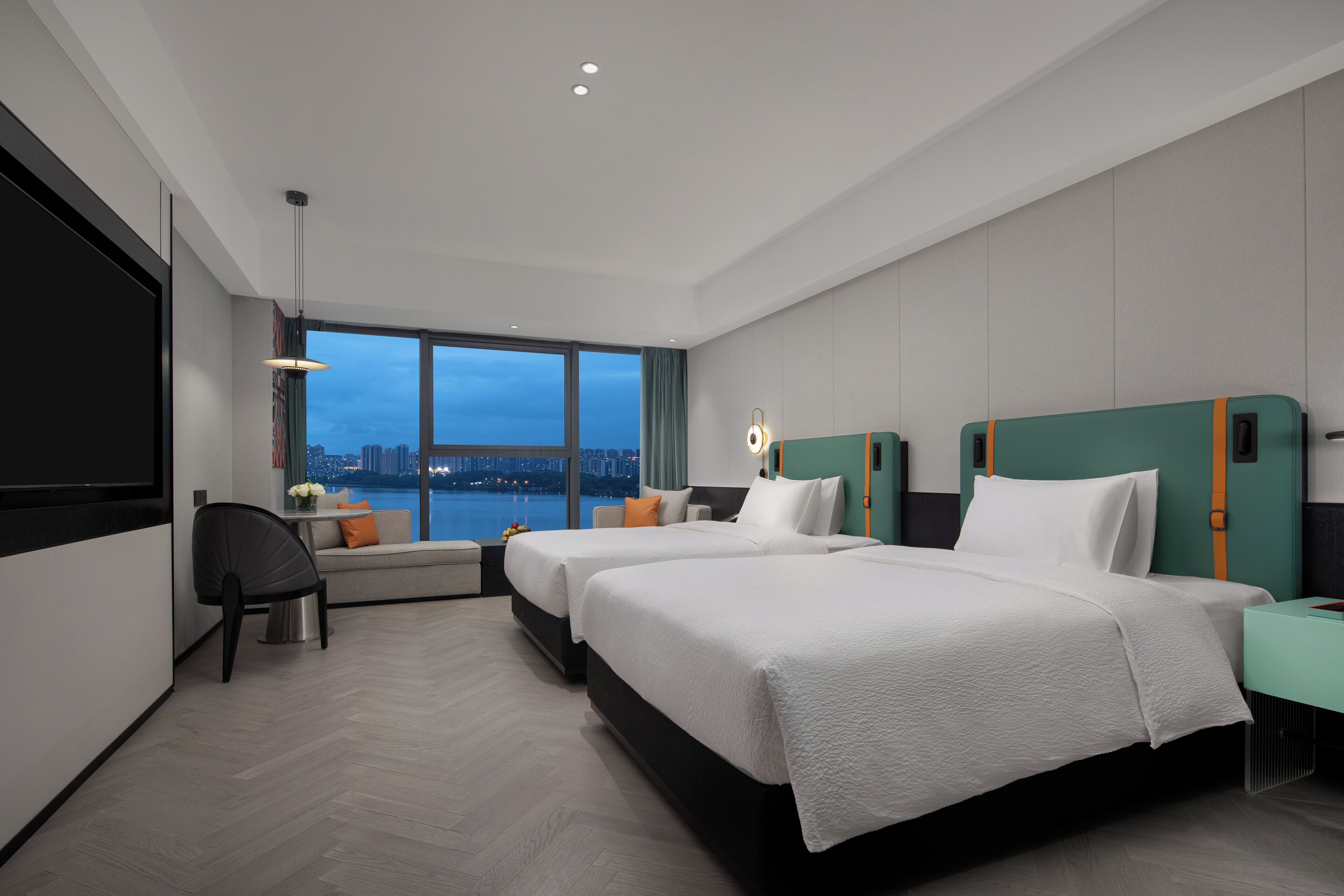 Una habitación de hotel moderna con dos camas, un área de estar, televisión y vista a la ciudad.
