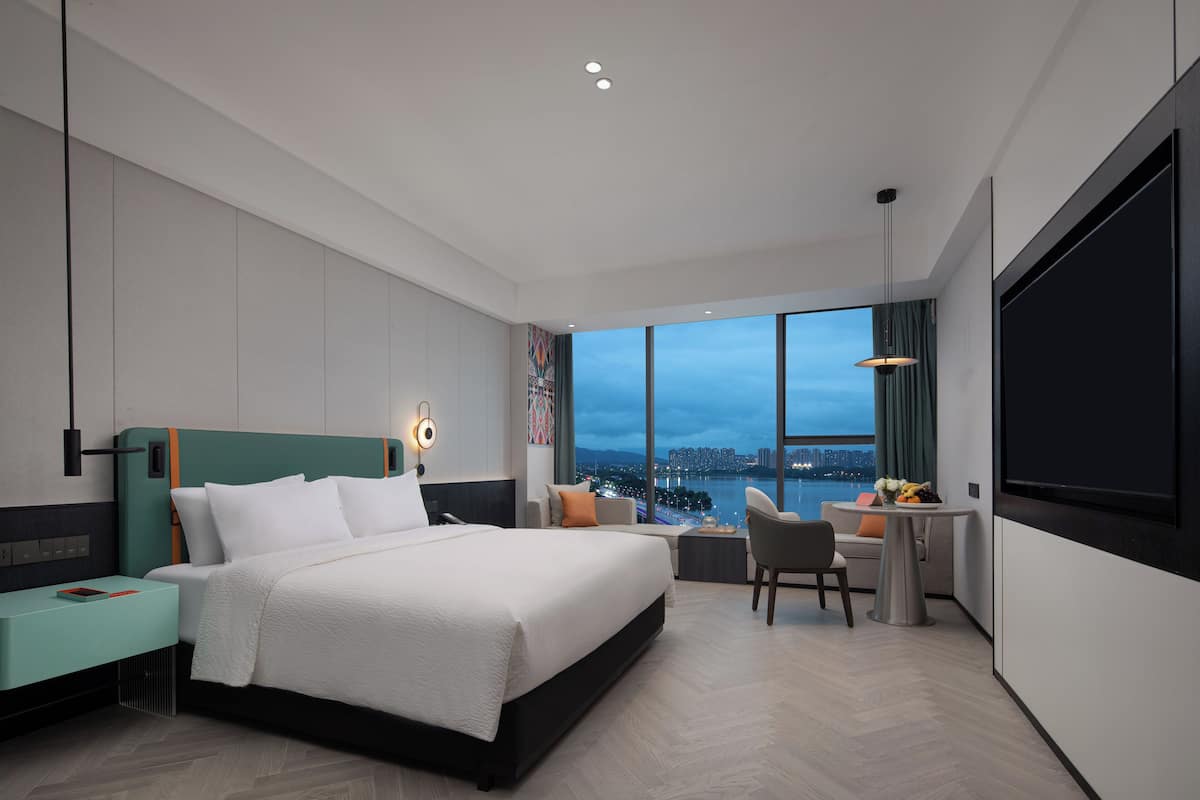 Ein modernes Hotelzimmer mit einem großen Bett, einem Schreibtisch und Blick auf die Stadt.