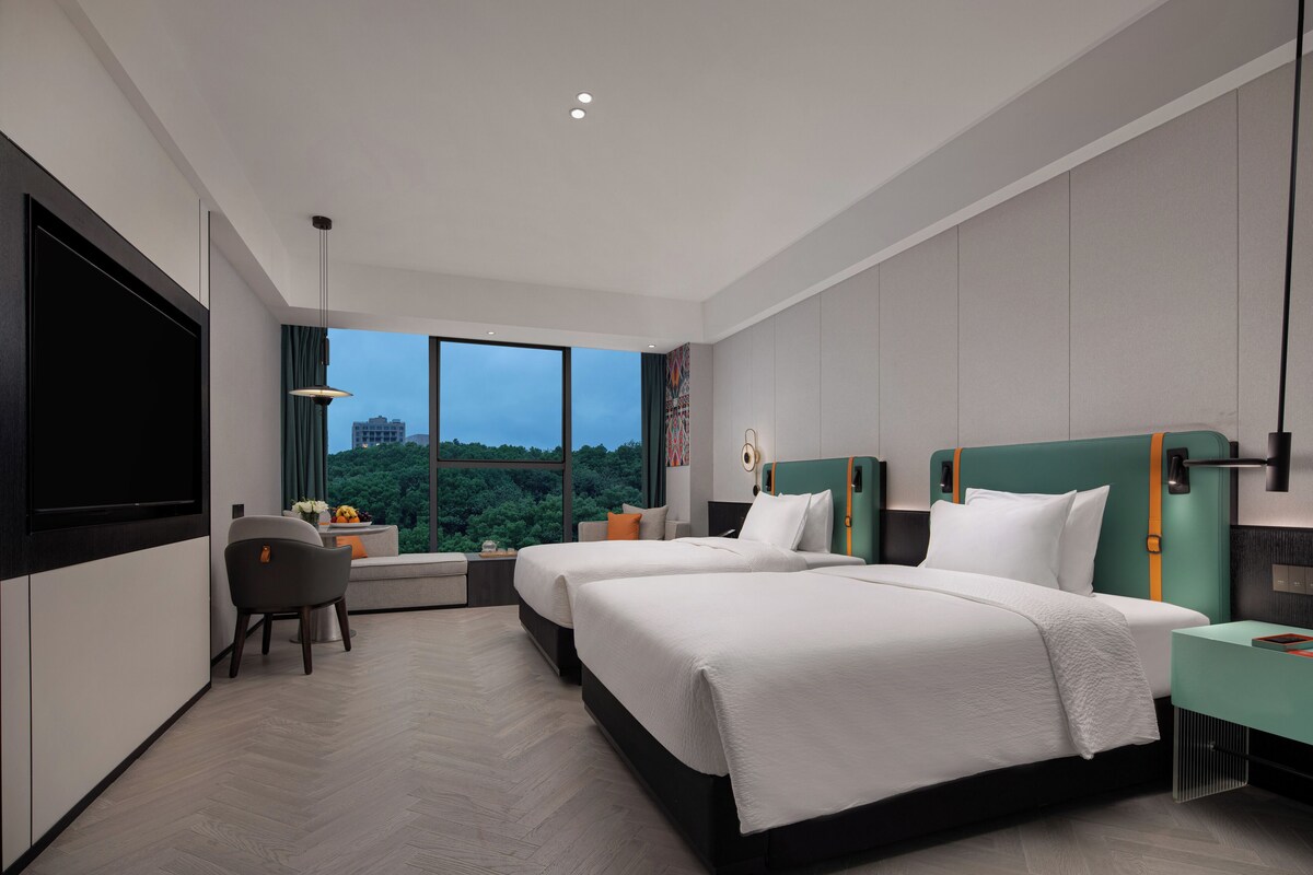 A modern hotel room with a large bed, a desk, and a view of the cityscape.