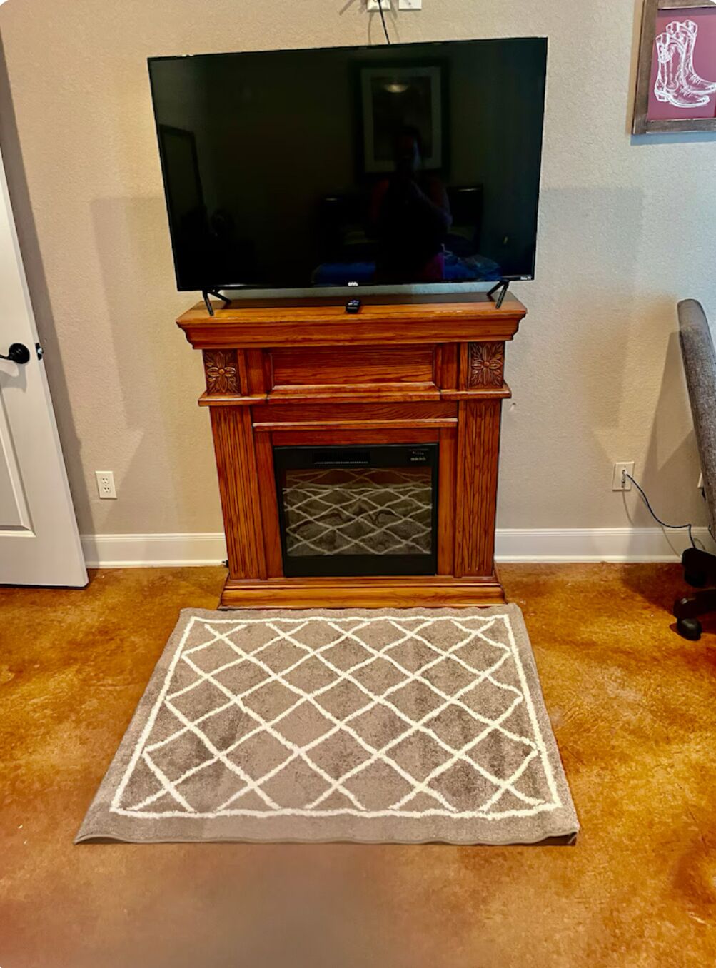 Une cheminée avec un téléviseur fixé au-dessus, un tapis à motifs devant, et une porte sur le côté gauche.