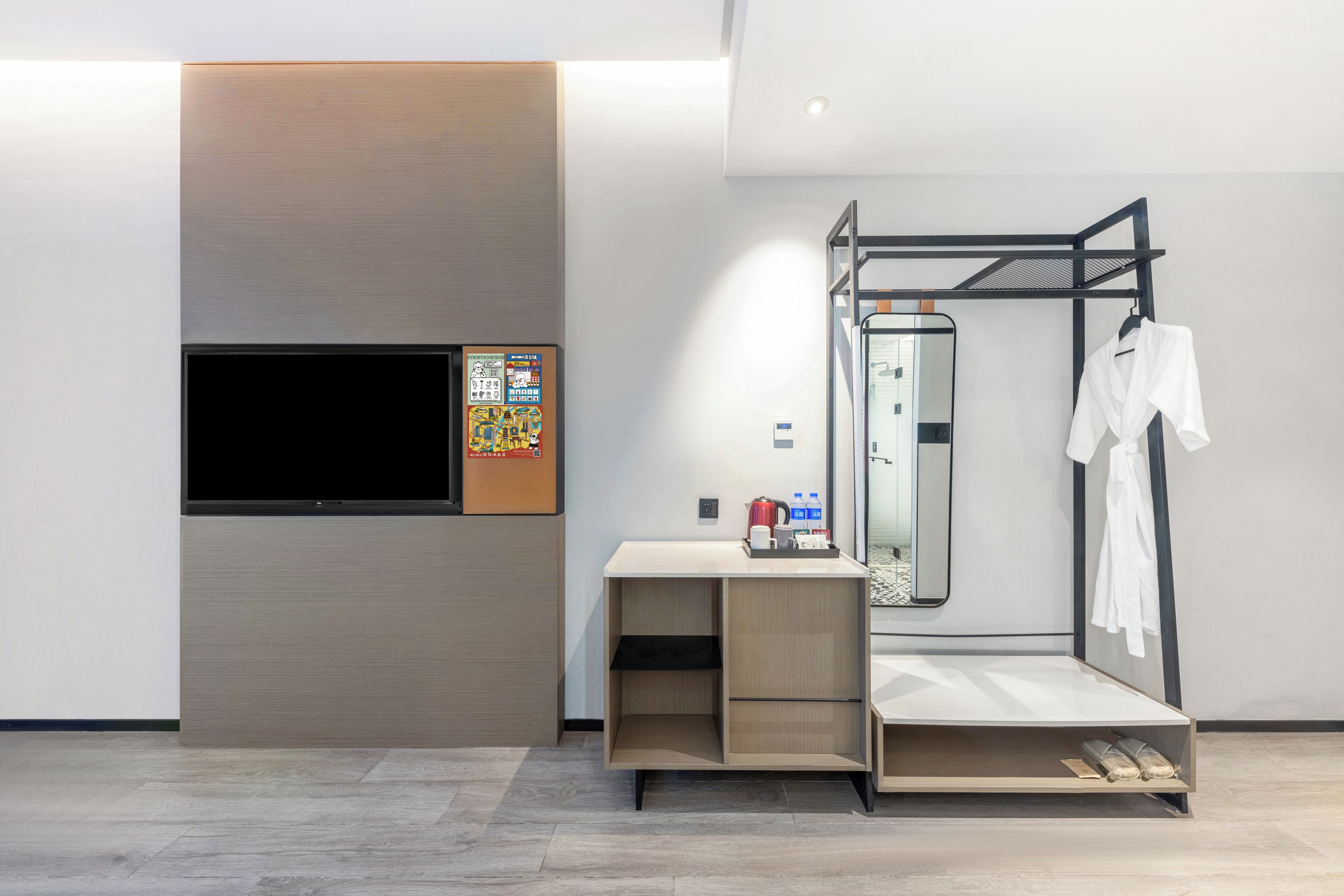 Habitación de hotel moderna con televisión de pantalla plana, una consola de madera, un espejo y un perchero metálico con una bata blanca.