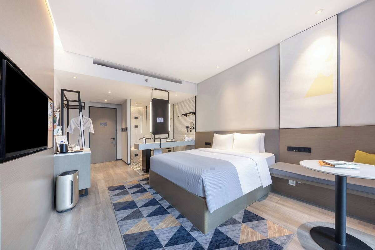 Ett modernt hotellrum med en stor säng, ett nattduksbord, en tv och ett badrum som syns genom en öppen dörr.