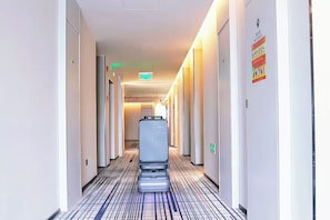 Pasillo de hotel con un ascensor central, puertas a ambos lados y suelo estampado.