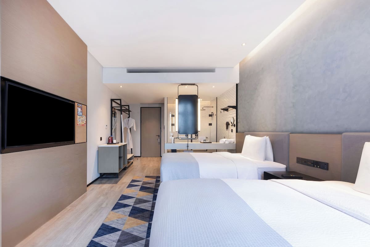 Ett hotellrum med två sängar, en TV, ett badrum och en hall som leder till en dörr.