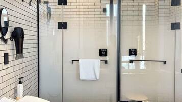 Un baño moderno con cabina de ducha de vidrio, un perchero y una bandeja con vasos.