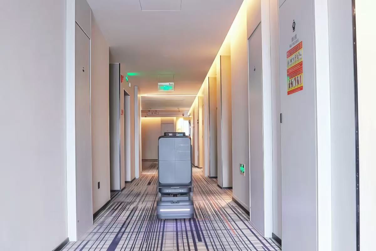 Un pasillo de hotel con un ascensor automático, puertas a ambos lados y piso estampado.