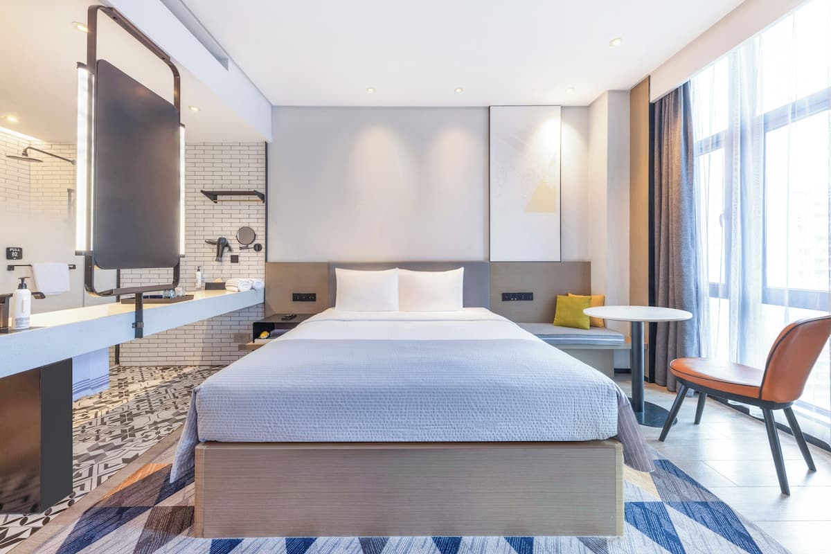 Ett modernt hotellrum med en stor säng, ett sängbord, en stol och ett litet runt bord.