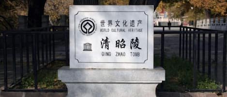 Un monumento de piedra con inscripciones, rodeado por una cerca de metal negro y árboles al fondo.