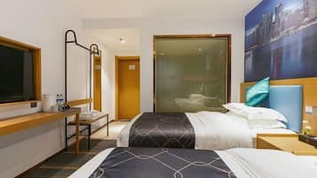 A hotel room with two beds, a desk, a chair, a large window, and a cityscape painting.