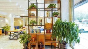 A modern interior with a wooden bookshelf filled with plants and books, a dining area with a table and chairs, and a view of the street outside. - Chonpines Hotel (Shengyang Provincial Government, Changjiang North Street, Beilin) (Shenyang)