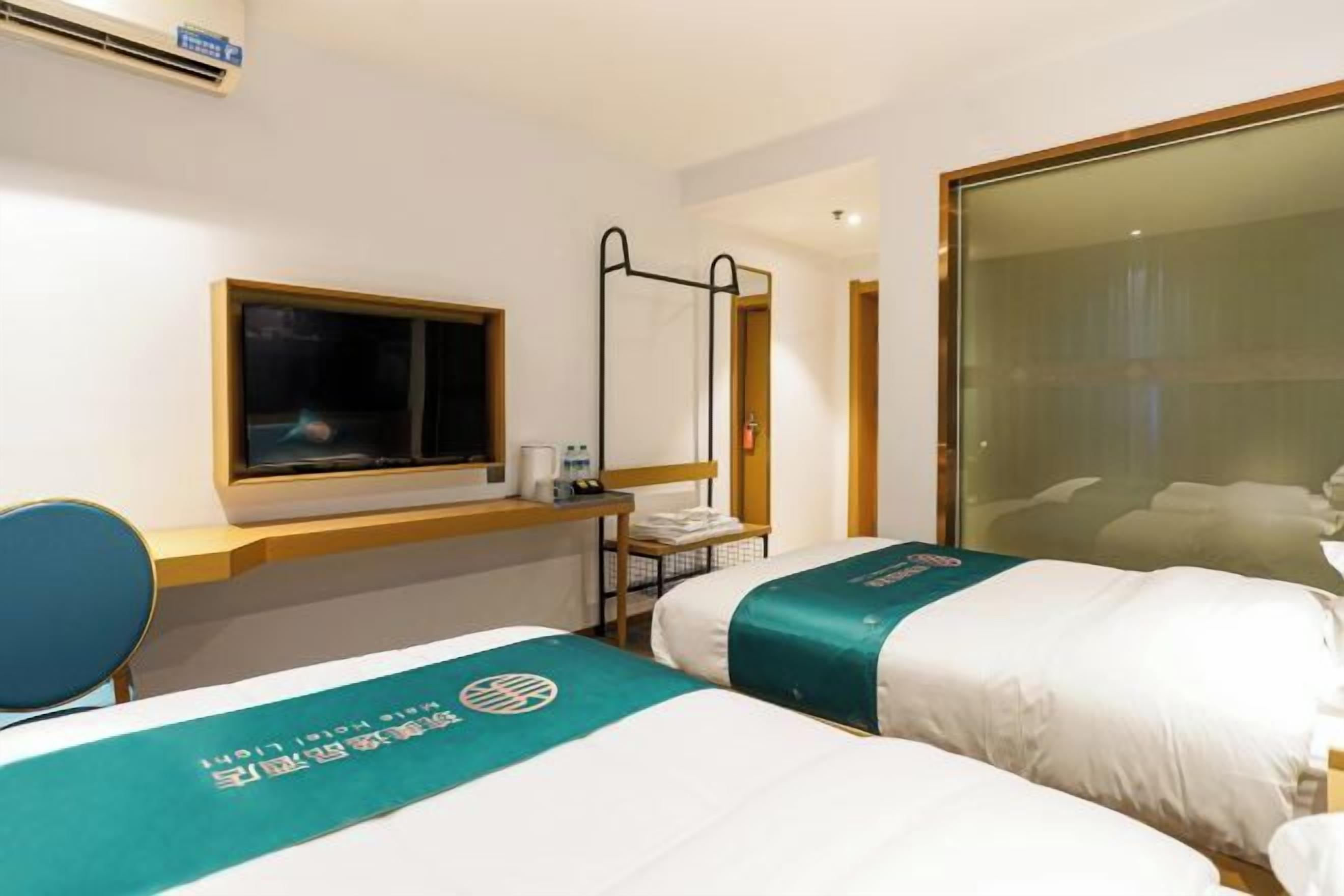 A hotel room with two beds, a desk, a chair, a window, and a mirror.