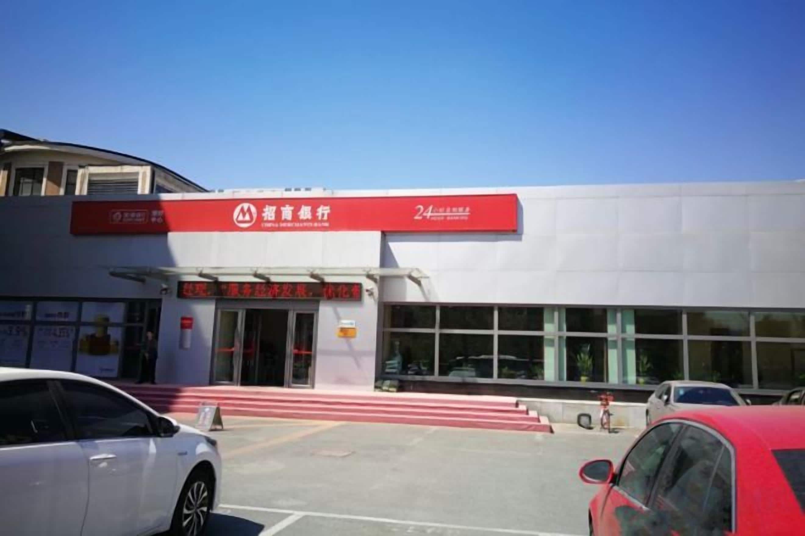 A building with a red sign, a car parked in front, and a clear sky.