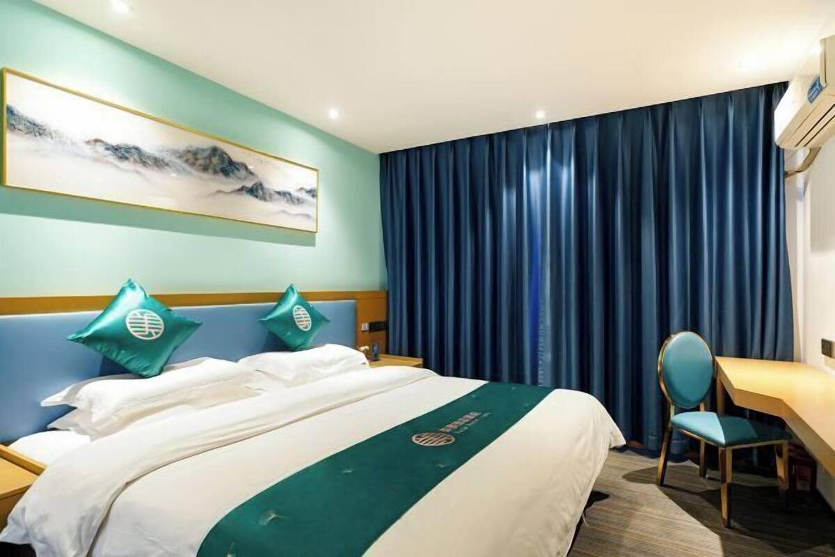 A hotel room with a bed, a desk, a chair, a painting on the wall, and a curtain.