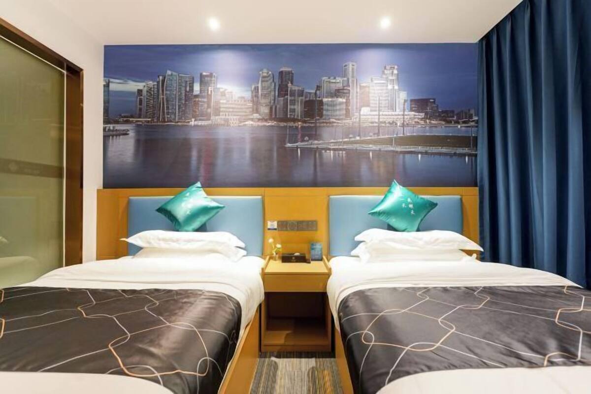 A hotel room with two beds, a cityscape mural, a nightstand, and a view of a body of water.