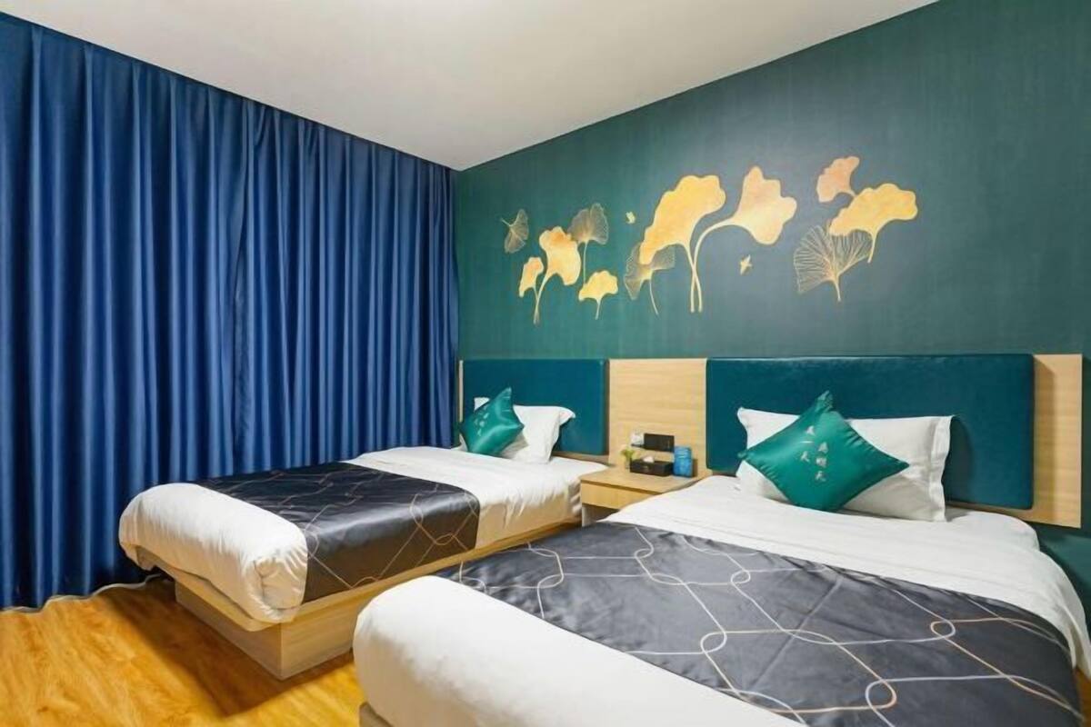 A hotel room with two beds, a wooden floor, a blue curtain, and a wall with a leaf pattern.