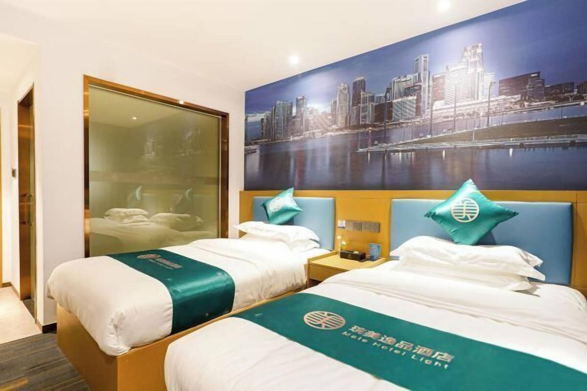 A hotel room with two beds, a cityscape mural, and a glass door leading to a balcony.