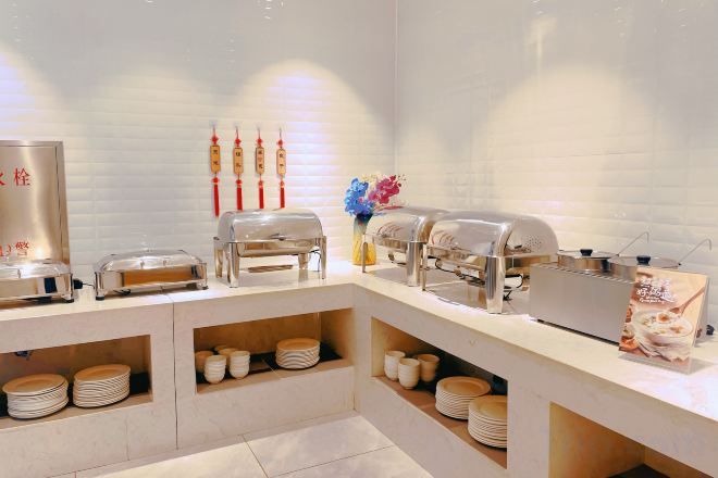 Montaje tipo bufé con múltiples estaciones de servicio, incluyendo opciones de comida caliente y fría, y una variedad de platos exhibidos en estanterías.