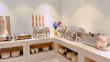 Montaje tipo bufé con múltiples estaciones de servicio, incluyendo opciones de comida caliente y fría, y una variedad de platos exhibidos en estanterías.