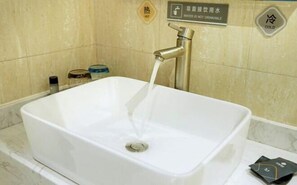 Bathroom features a large sink with running water, a tiled wall, and storage containers.