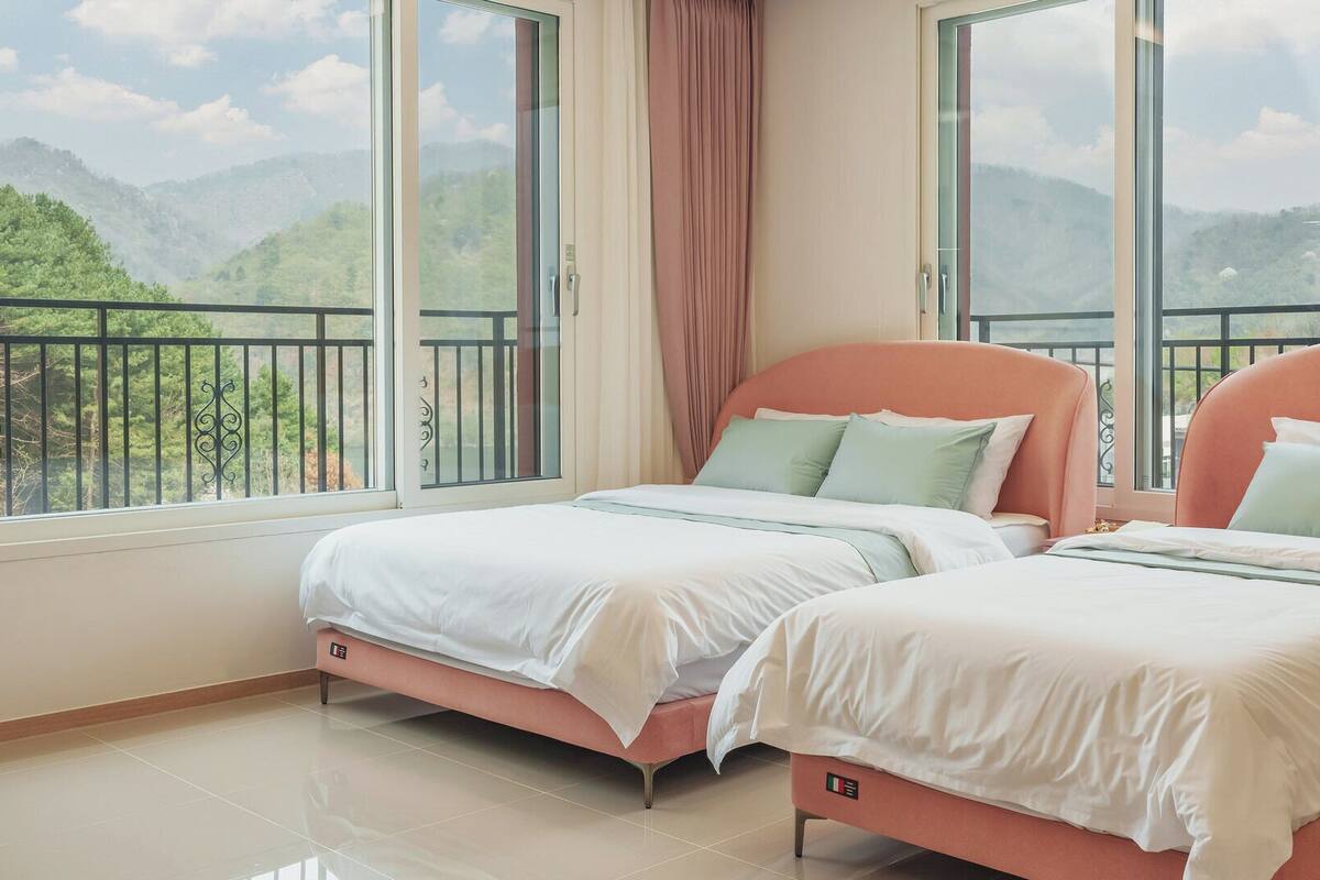 Un dormitorio con dos camas, ventanas amplias y un balcón con vistas a las montañas.