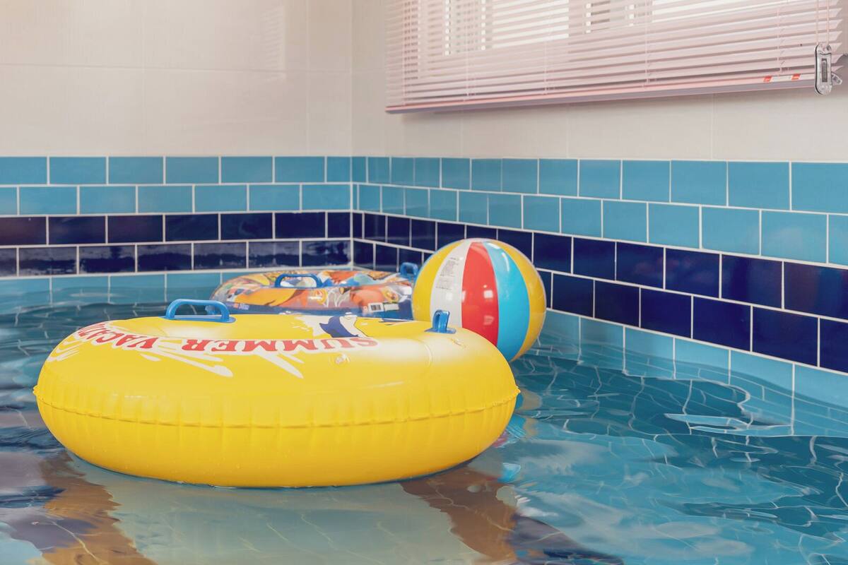 Una piscina interior con paredes de azulejos azules y un flotador inflable amarillo.