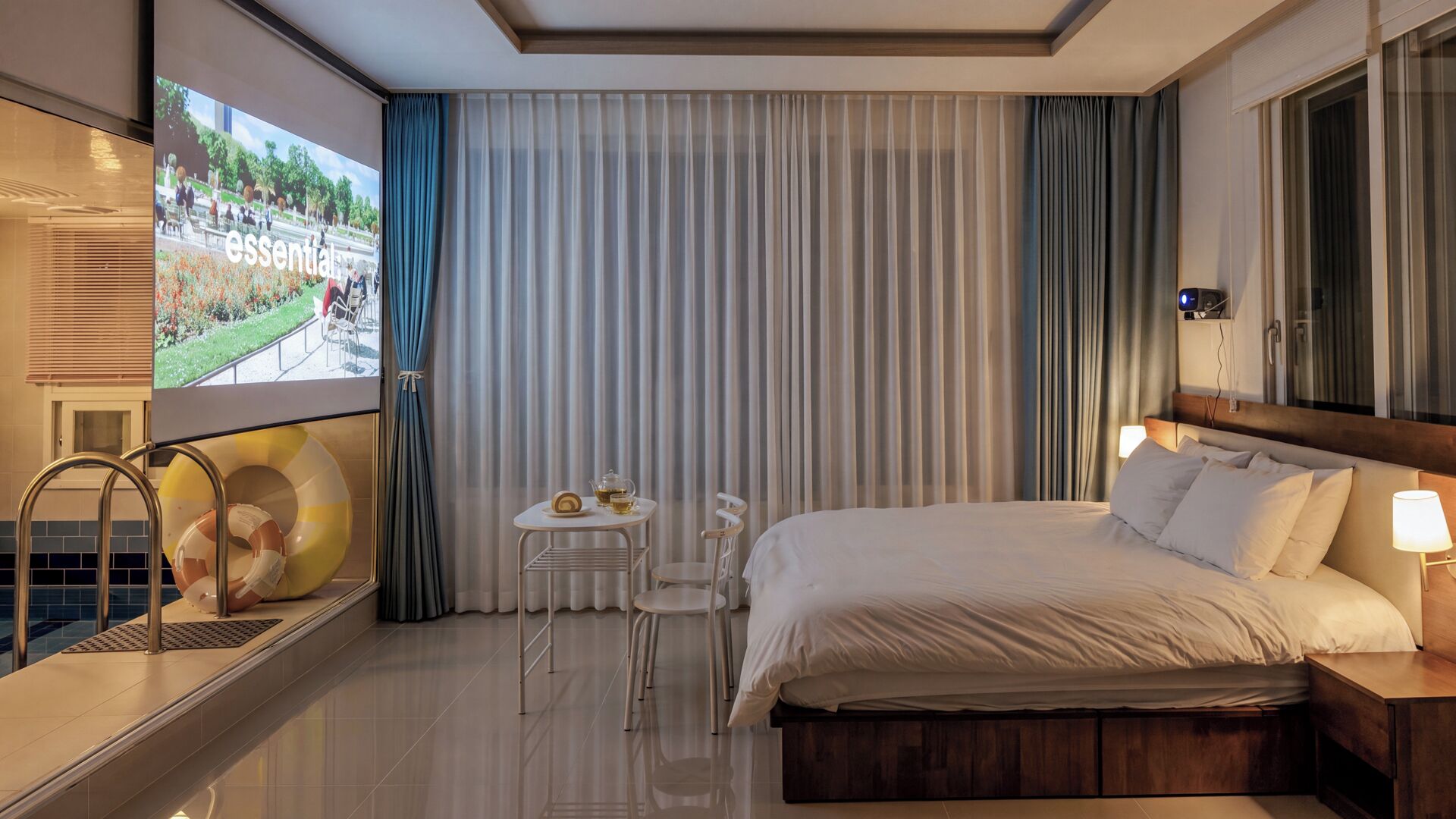 Habitación de hotel con cama, mesita de noche, lámpara, silla y vista a un jardín por la ventana.