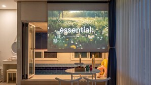 A modern kitchen with a large screen displaying 'essential' and a dining area with a table, chairs, and a small decorative item. - Gapyeong Reflex Pool Villa Pension (Gapyeong)